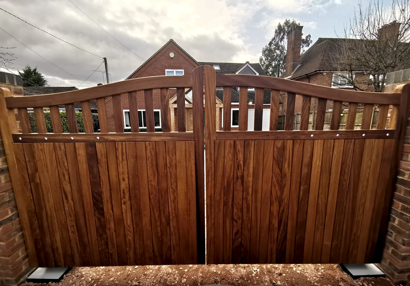 Bespoke automated hardwood double swing gate installed between brick piers