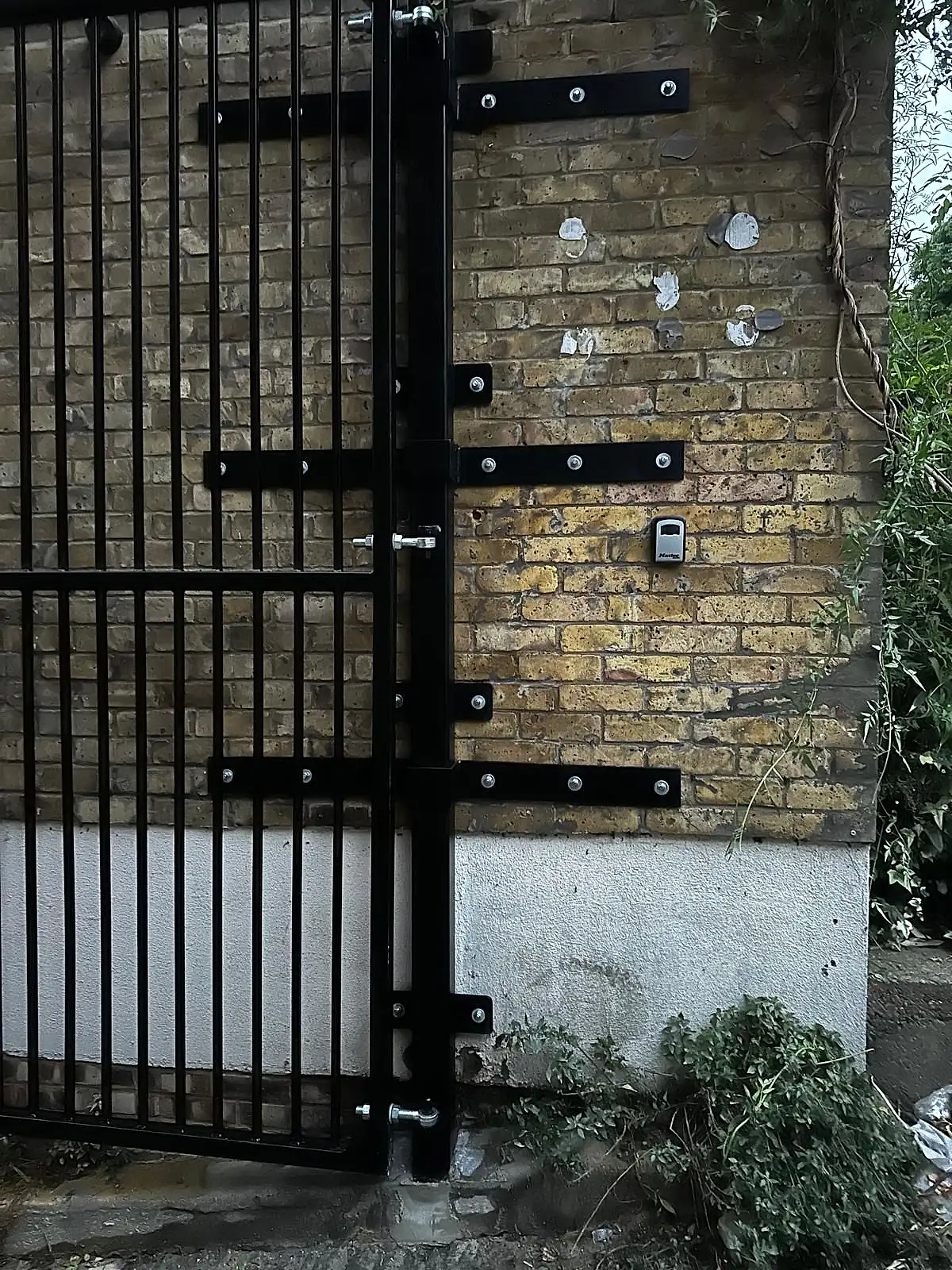 Bespoke black metal security gate with heavy-duty hinges fitted to a brick wall